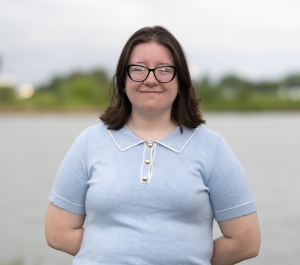 Woman in a light blue short sleeve sweater and dark rimmed glasses with shoulder length dark brown hair